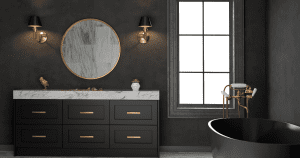 A modern bathroom designed for home remodeling near Rockford, Illinois, showcases dark walls and a black vanity with a marble countertop accented in gold. A round mirror is flanked by sconces above, and a black freestanding bathtub enjoys natural light from the large window. A small plant adorns the counter.