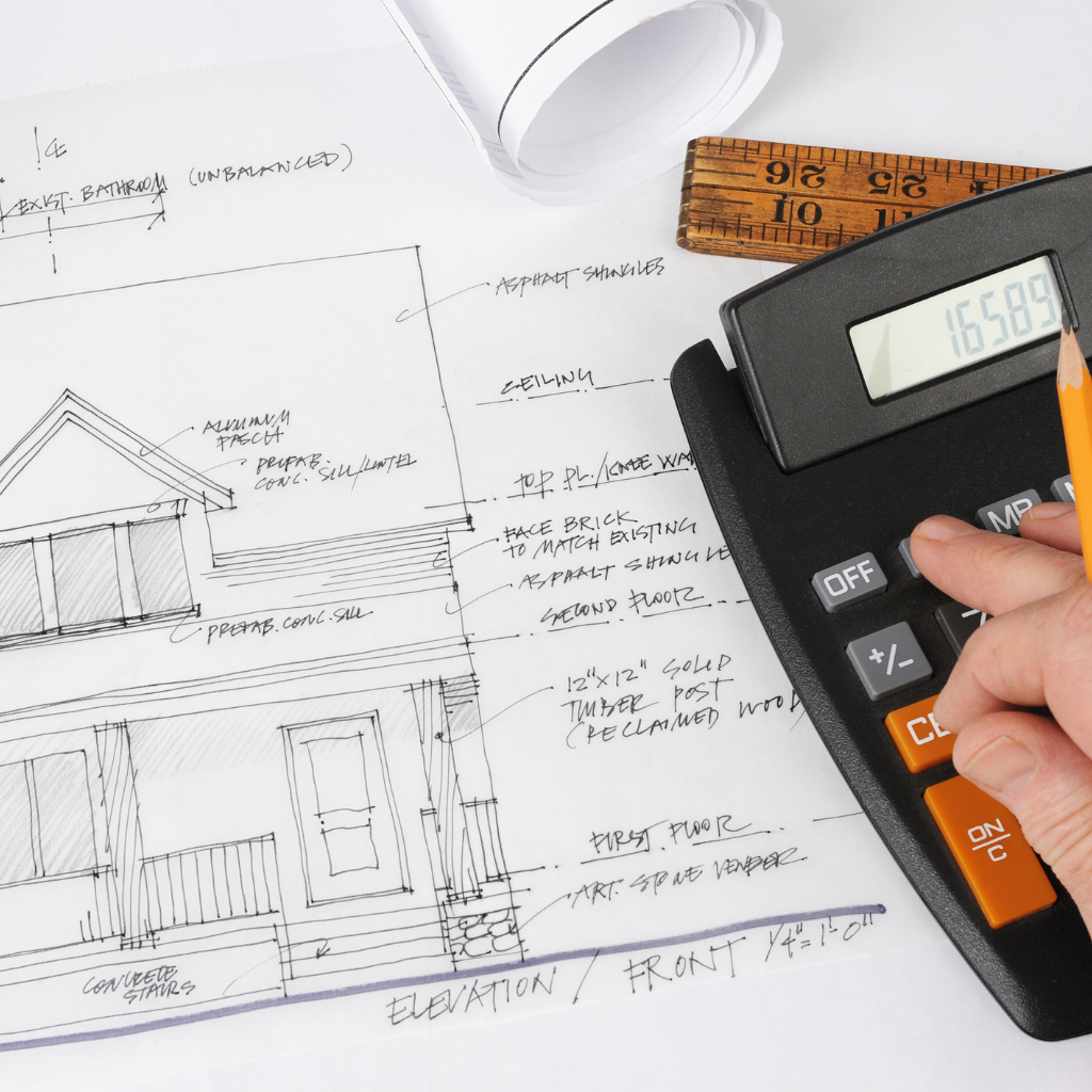 A hand holds a pencil near a calculator displaying "16589" next to an architectural drawing of a house. The drawing includes detailed notes and measurements. A wooden ruler and a rolled paper sit nearby on the desk.